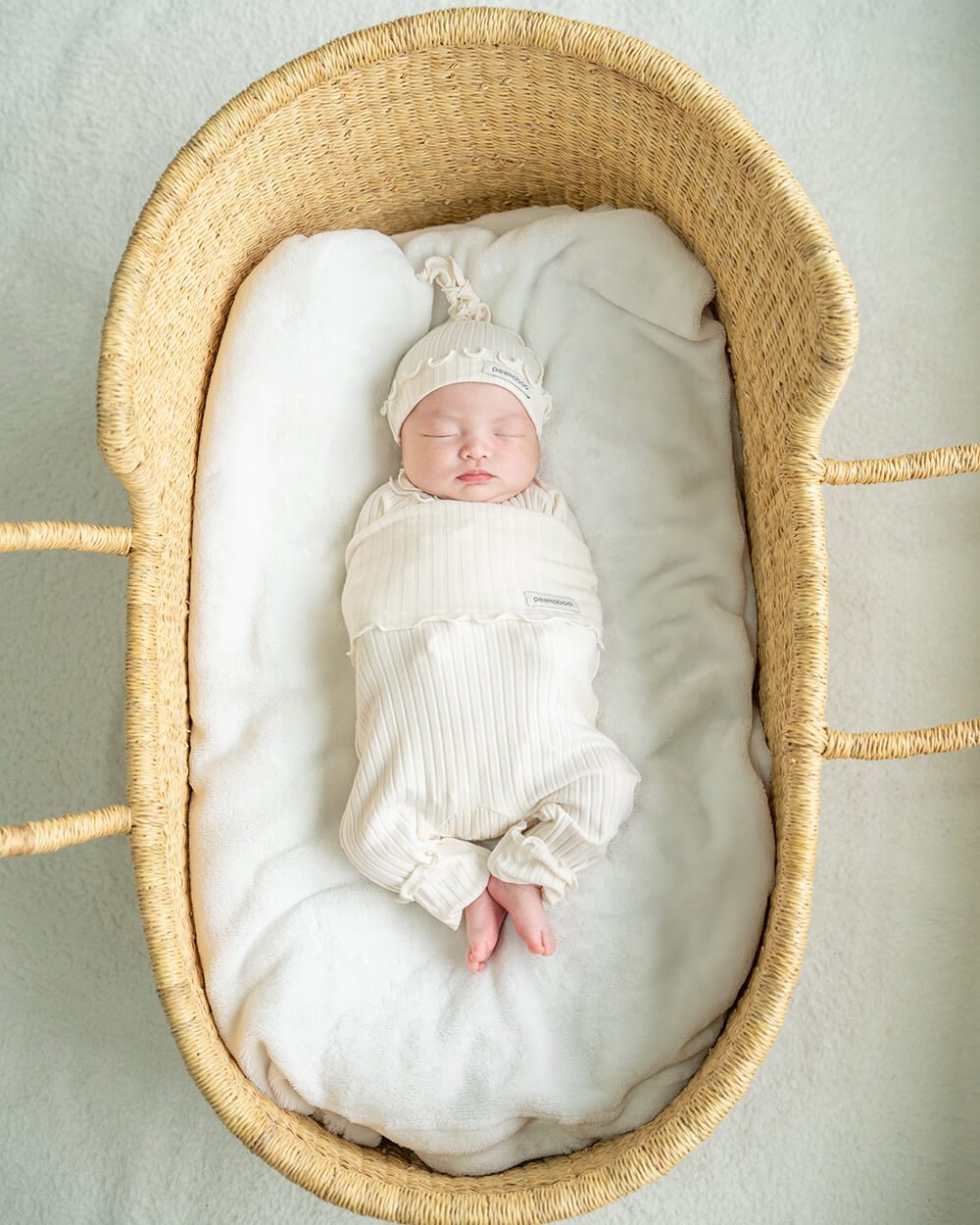 リブ素材のフリル付きニューボーンセットでかごの中で眠る新生児